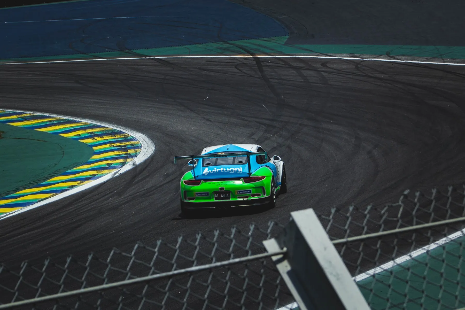 Porsche verde e azul contornando a curva sobre a zebra
