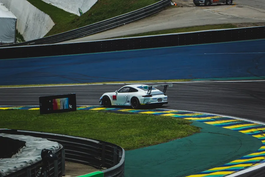 Carro branco contornando a curva, com grama e zebra em primeiro plano