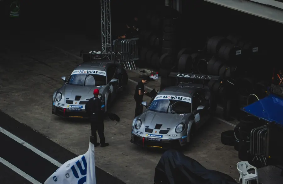 Vista de cima de dois carros prateados no box, cercados por pneus e equipe