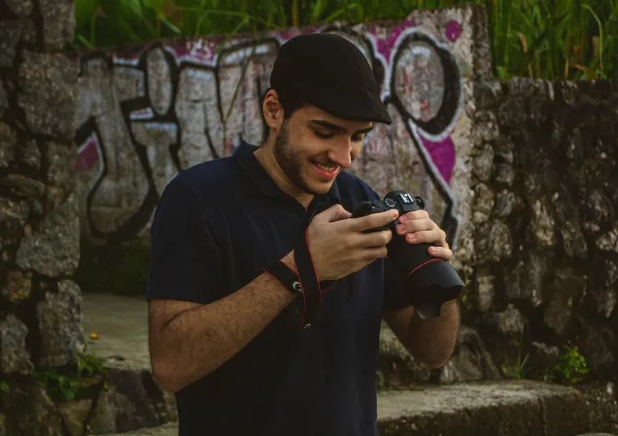 Fotógrafo sorrindo enquanto confere a câmera, com muro grafitado ao fundo
