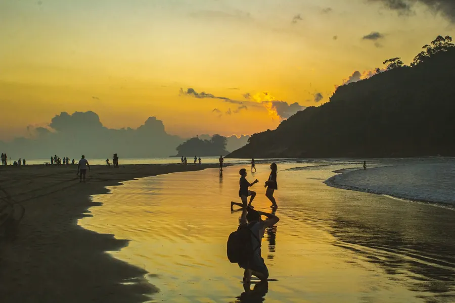Silhuetas na beira do mar refletidas na água dourada do pôr do sol